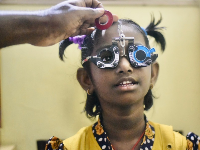 Young girl undergoing eye examination with trial lens frame.